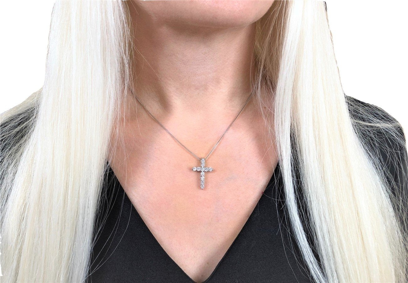 Person wearing a necklace with a cross pendant against a neutral background