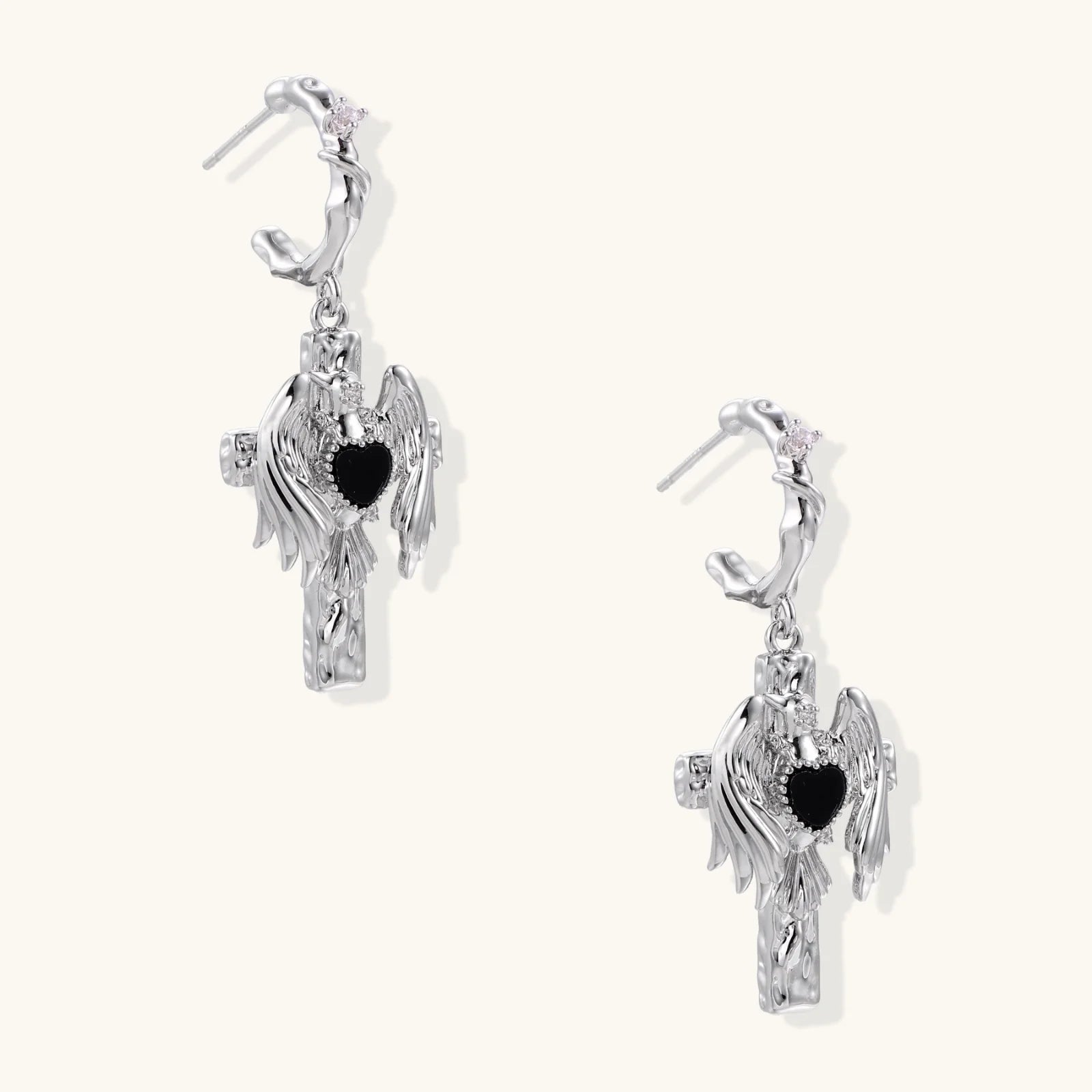 Silver drop earrings with twisted hoops and angel wings embracing black heart locket on white background.