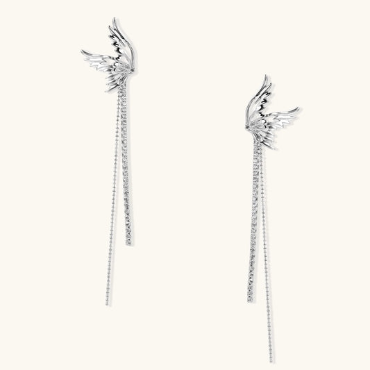 Pair of silver wing-shaped earrings with feather details and long sparkling crystal chain drops on cream background