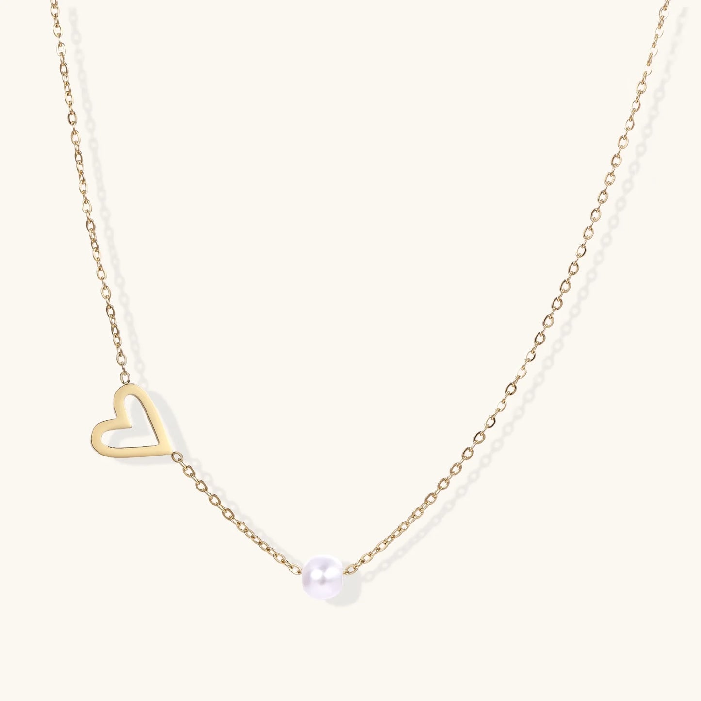 Delicate gold necklace with open heart charm and white pearl bead on fine chain against cream background