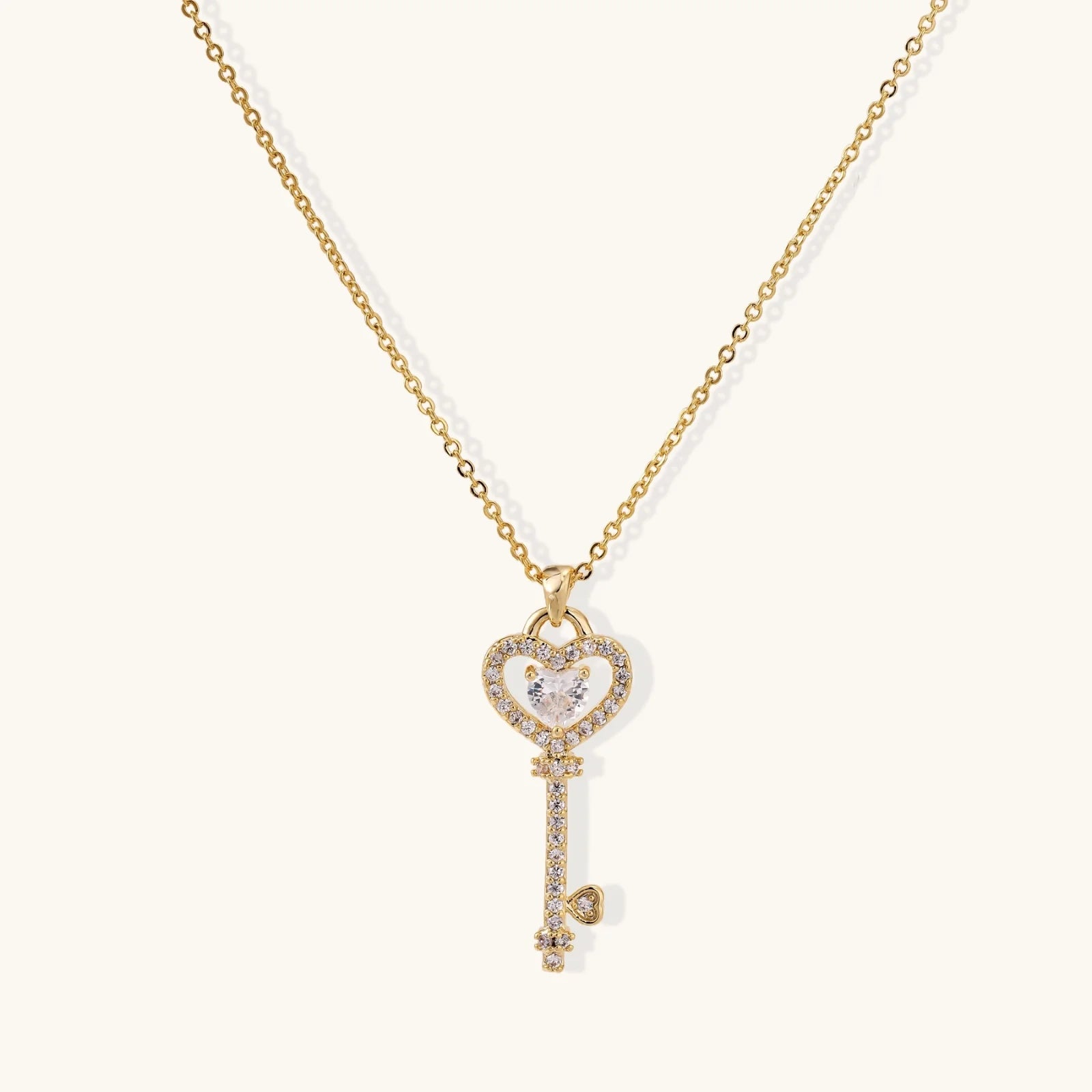 Delicate gold key pendant with heart-shaped bow and crystal pavé detailing on fine chain against cream background,  a perfect envouragement jewelry gift for women 