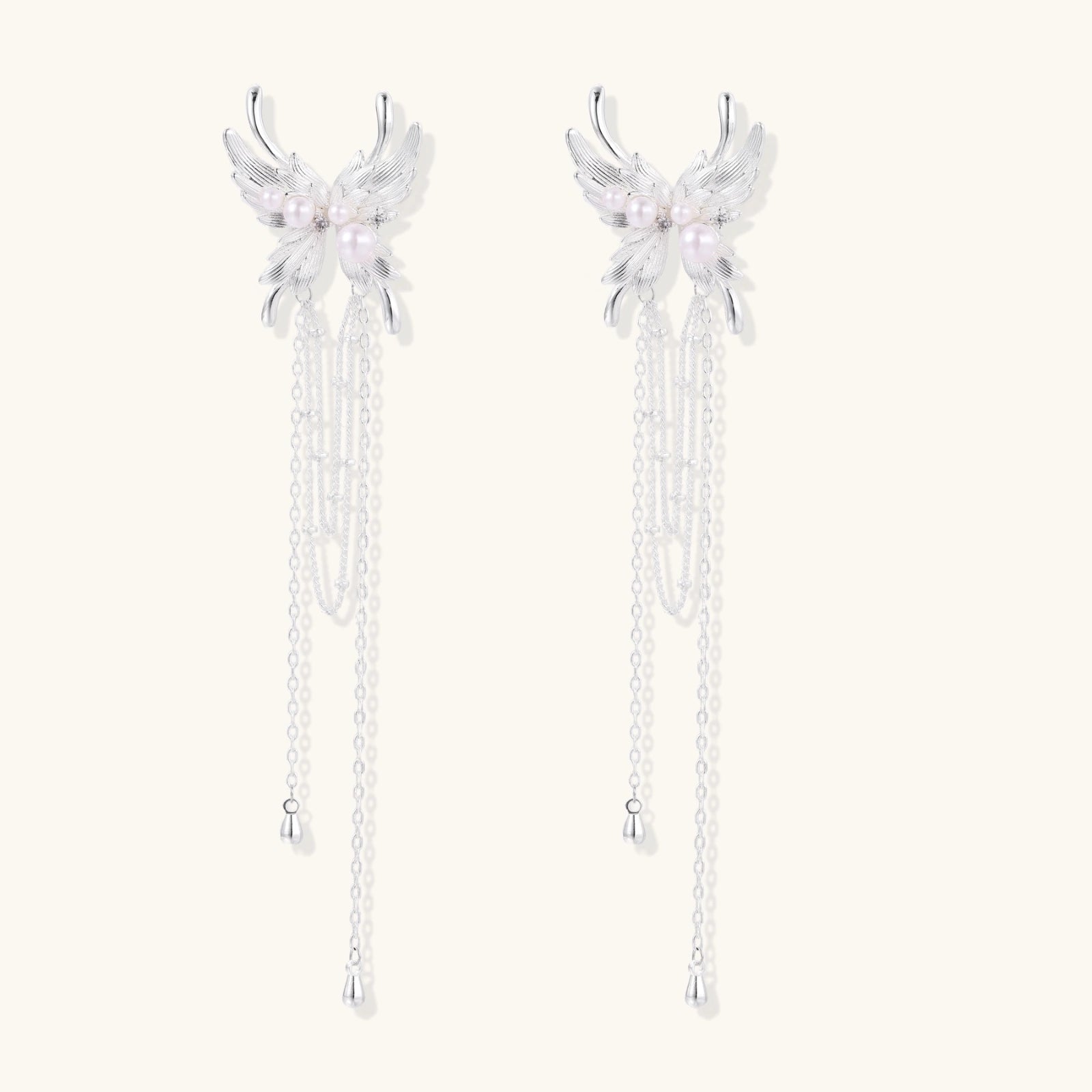 Elegant chandelier earrings with phoenix wing design, white pearls, and cascading silver chains on cream background