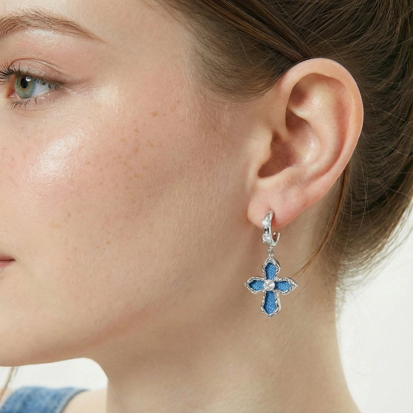 Close-up of a woman wearing a blue denim cross earring.