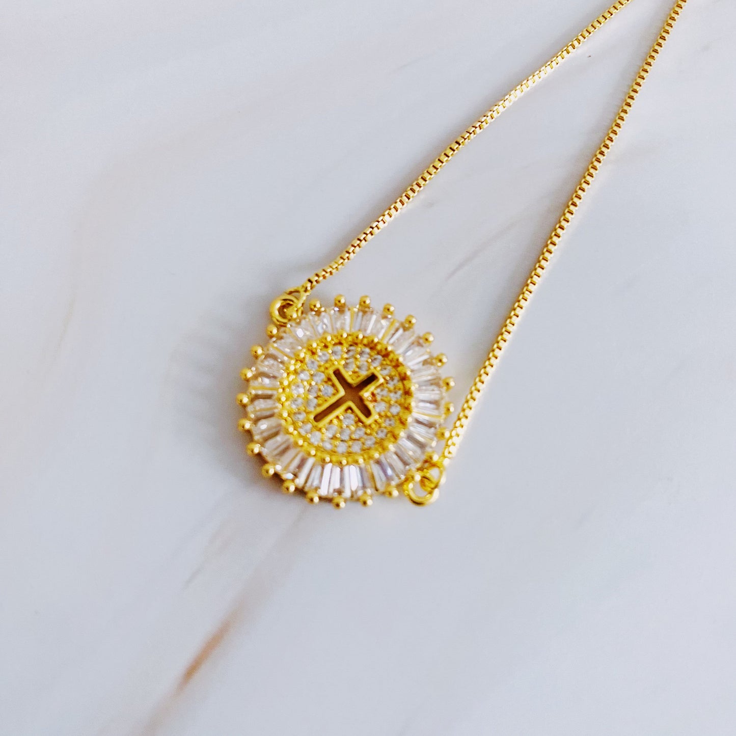 Gold necklace with a circular pendant featuring a cross on a light background