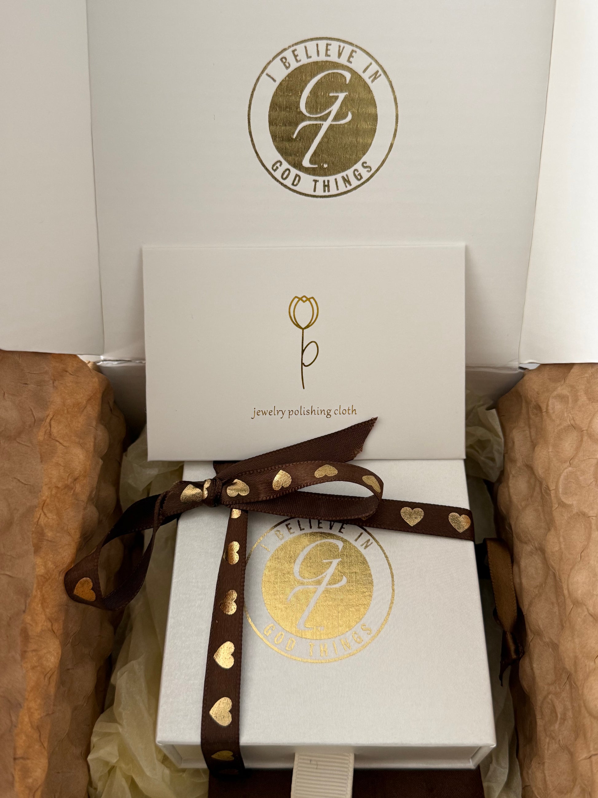 Jewelry packaging with gold logo and brown ribbon on a white box.