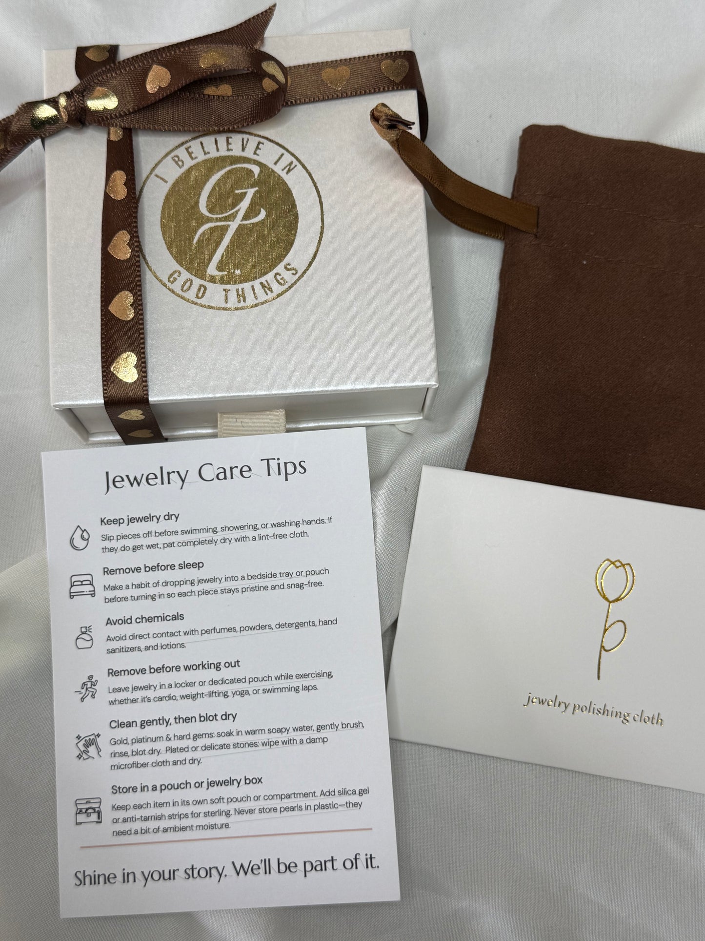 Jewelry box with gold ribbon, care card, and information sheet on a white background