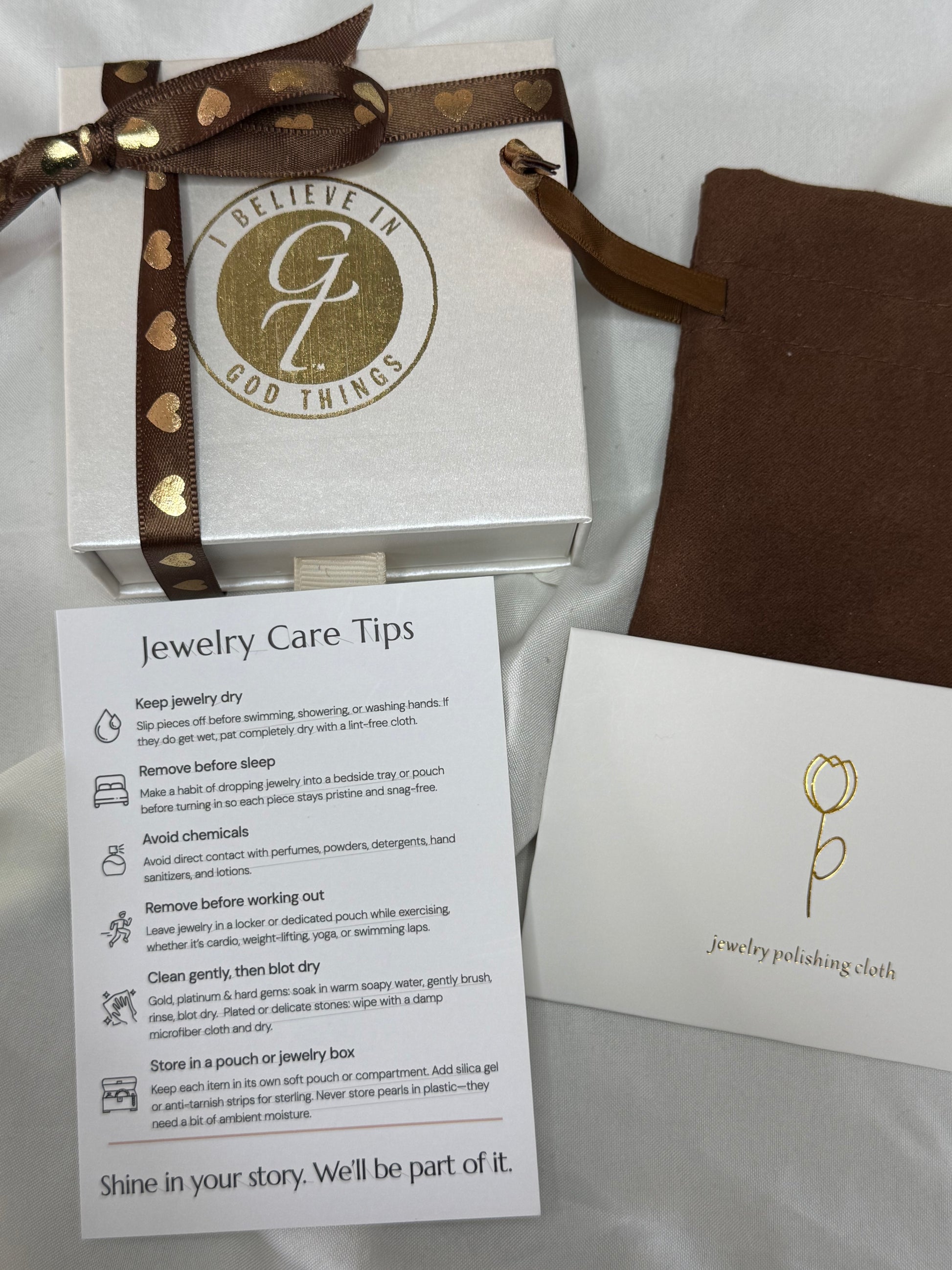 Jewelry box with gold ribbon, care card, and information sheet on a white background