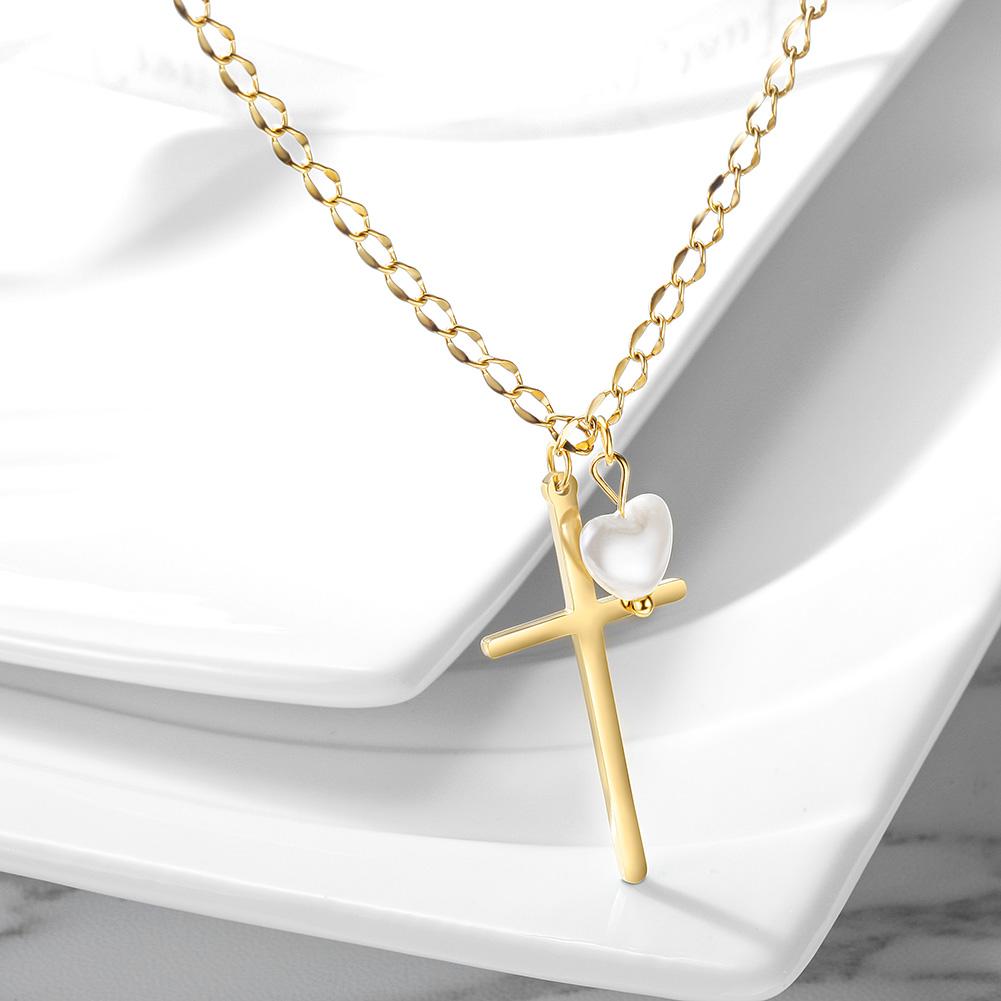 Gold necklace with a cross and heart pendant on a white surface