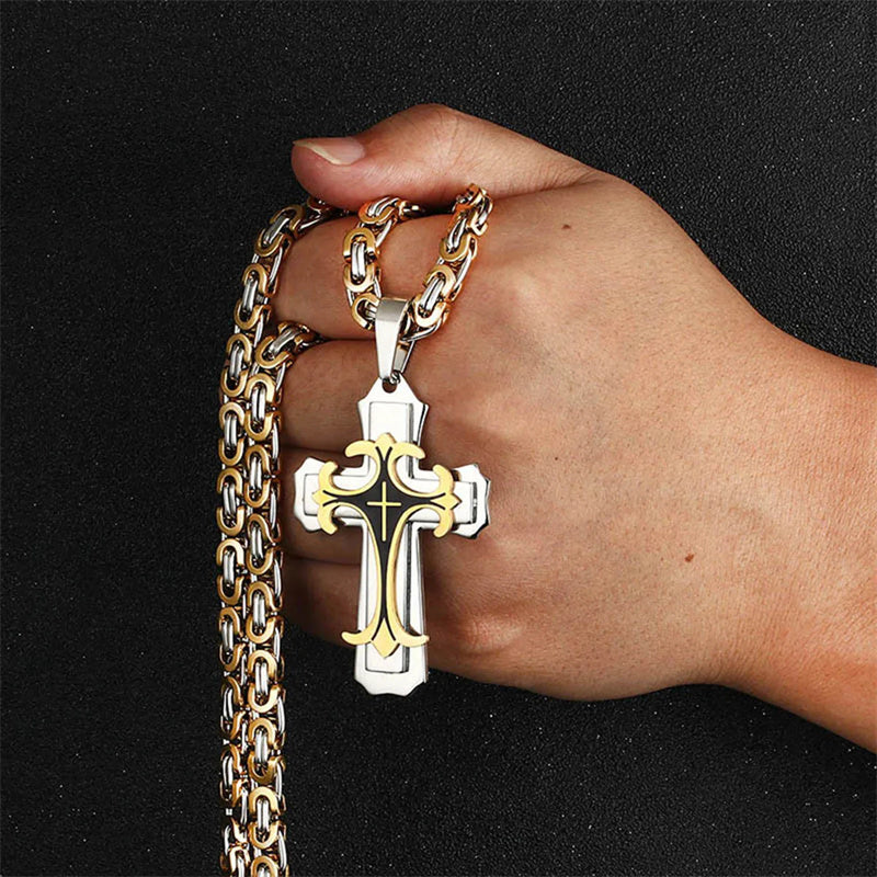Hand wearing a gold chain with a silver cross pendant on a black background