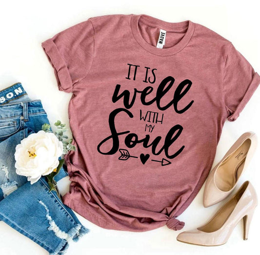 Mauve t-shirt with 'It is well with my soul' text, jeans, and high heels on a white background