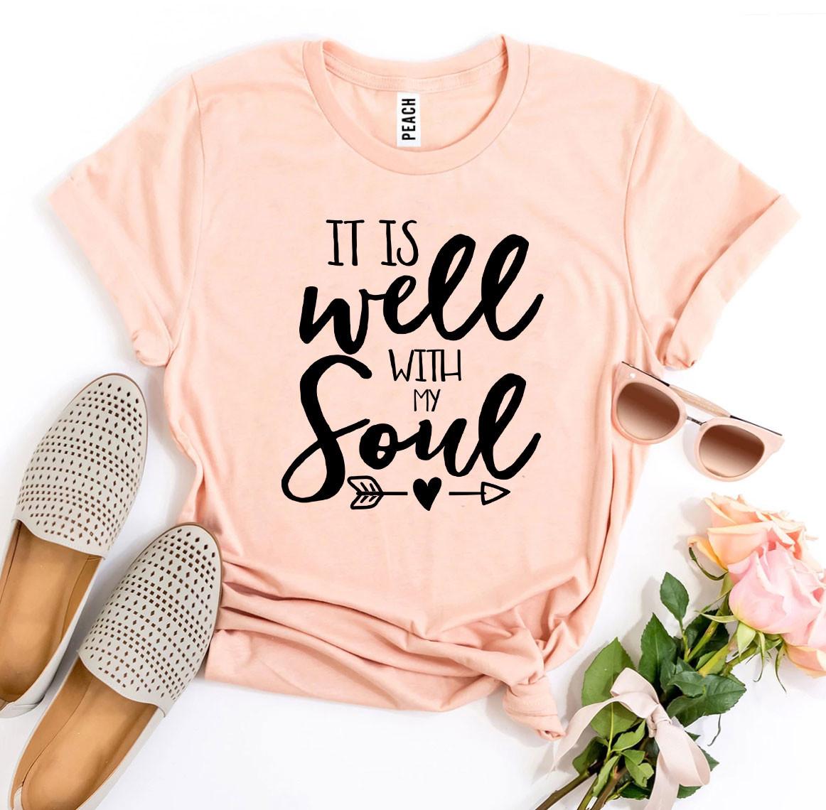 Peach t-shirt with 'It is well with my soul' text, accompanied by shoes, sunglasses, and flowers on a white background.