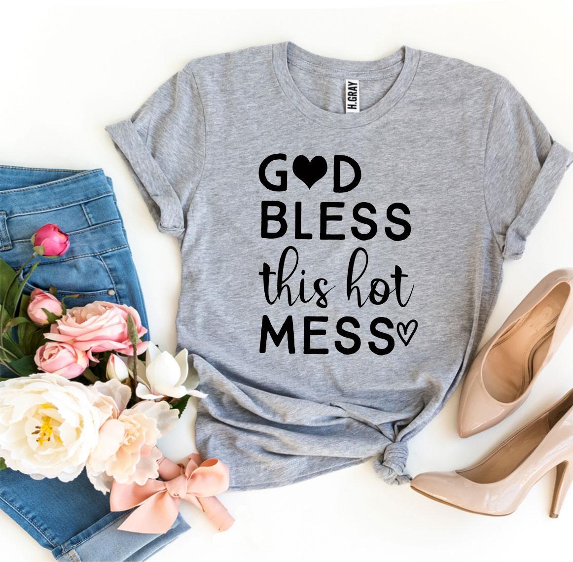 Gray t-shirt with 'God bless this hot mess' text, paired with jeans, shoes, and flowers on a white background